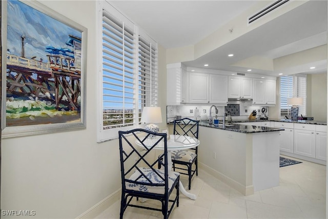 kitchen featuring white cabinetry, tasteful backsplash, kitchen peninsula, dark stone counters, and light tile patterned floors