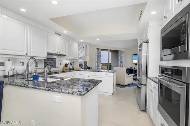 kitchen with stainless steel appliances, a peninsula, white cabinetry, recessed lighting, and dark stone counters