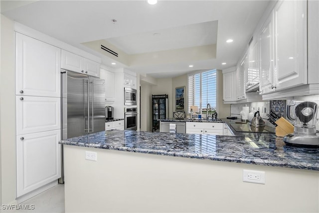 kitchen featuring dark stone countertops, a tray ceiling, white cabinetry, kitchen peninsula, and stainless steel appliances