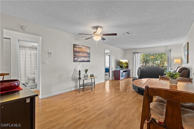 living room with ceiling fan, light hardwood / wood-style flooring, and a textured ceiling