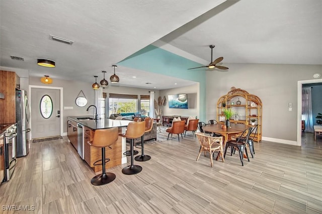 kitchen featuring appliances with stainless steel finishes, a kitchen breakfast bar, ceiling fan, sink, and an island with sink