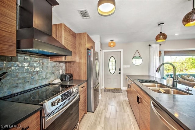 kitchen featuring decorative backsplash, appliances with stainless steel finishes, sink, wall chimney range hood, and decorative light fixtures