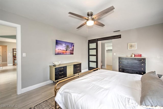 bedroom featuring hardwood / wood-style floors, ceiling fan, and a barn door