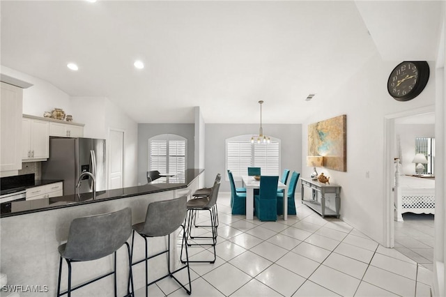 kitchen with hanging light fixtures, white cabinets, stainless steel refrigerator with ice dispenser, a kitchen bar, and light tile patterned floors