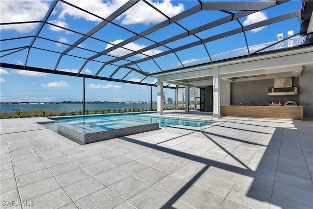 view of pool featuring glass enclosure, a water view, exterior kitchen, and a patio