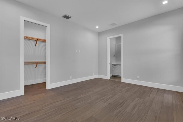 unfurnished bedroom featuring hardwood / wood-style floors, ensuite bathroom, a spacious closet, and a closet