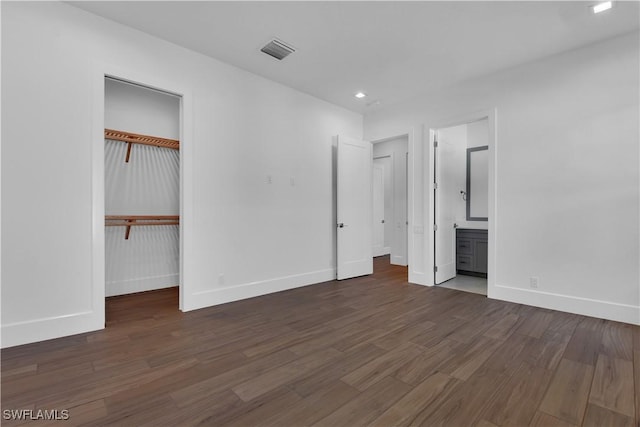 unfurnished bedroom with ensuite bath, a closet, and dark hardwood / wood-style flooring