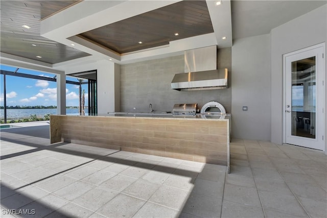 kitchen featuring sink, wooden ceiling, wall chimney range hood, a raised ceiling, and a water view