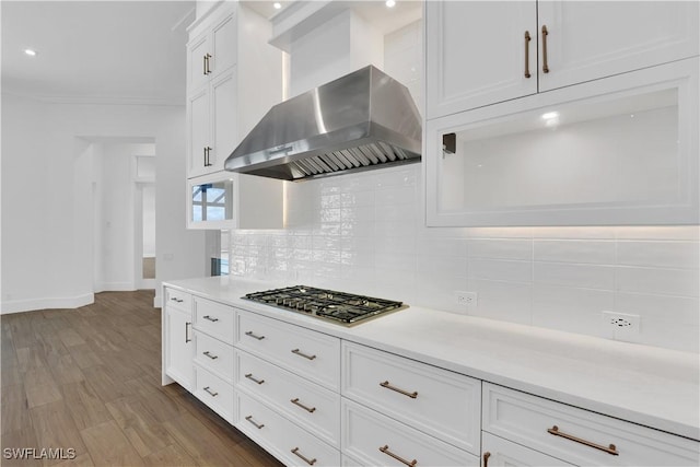 kitchen with wall chimney exhaust hood, tasteful backsplash, light hardwood / wood-style floors, stainless steel gas stovetop, and white cabinets