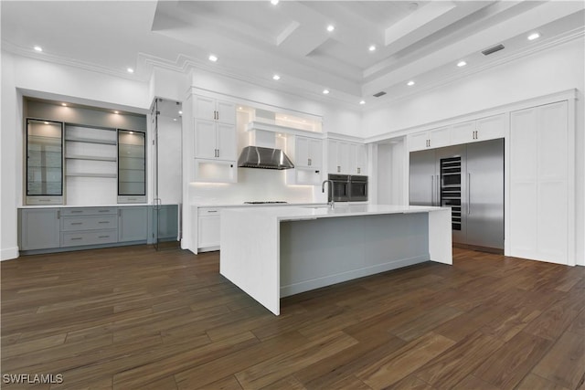 kitchen with a high ceiling, built in fridge, range hood, an island with sink, and white cabinets