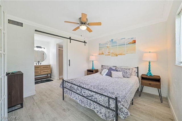 bedroom with a barn door, ceiling fan, crown molding, and light wood-type flooring