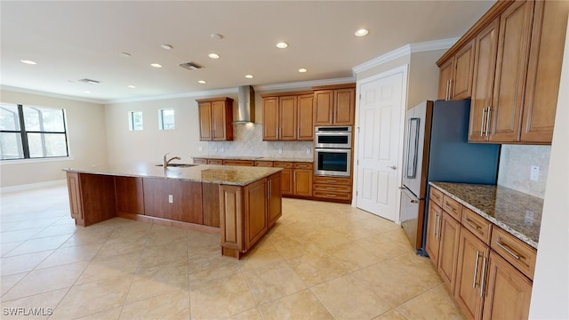 kitchen with a kitchen island with sink, wall chimney exhaust hood, light stone countertops, ornamental molding, and appliances with stainless steel finishes