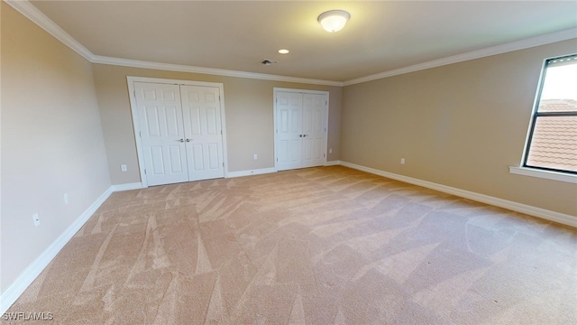 unfurnished bedroom featuring light carpet, multiple closets, and crown molding