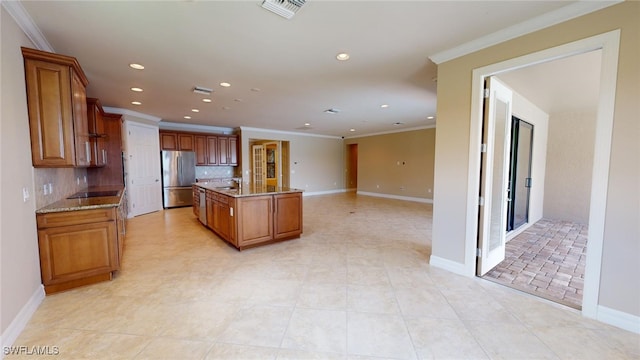 kitchen featuring stainless steel refrigerator, tasteful backsplash, an island with sink, black electric stovetop, and ornamental molding