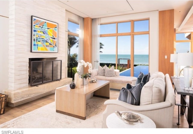 living room featuring a large fireplace, a water view, light hardwood / wood-style flooring, and floor to ceiling windows
