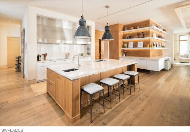 kitchen featuring sink, decorative light fixtures, light hardwood / wood-style flooring, light stone countertops, and a large island