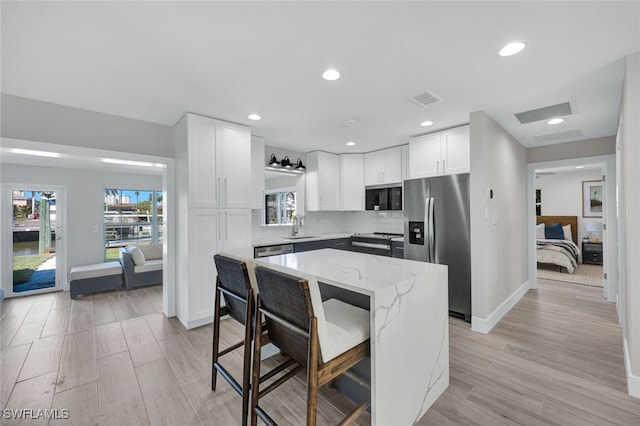 kitchen with sink, appliances with stainless steel finishes, white cabinetry, light stone countertops, and a kitchen island