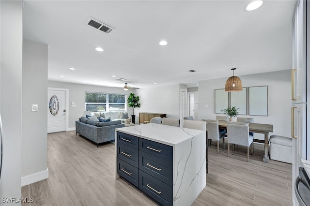 kitchen with light wood-type flooring, ceiling fan, hanging light fixtures, and light stone countertops