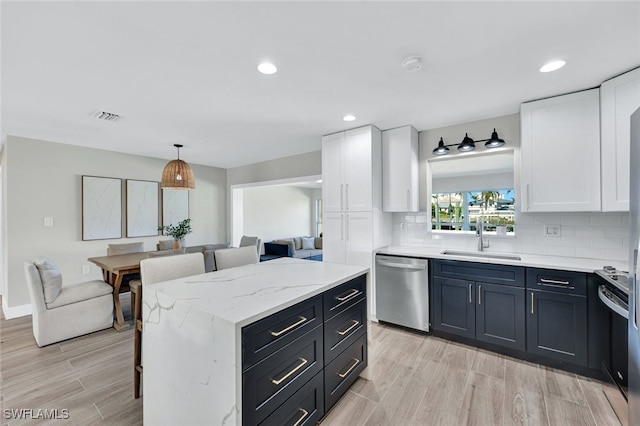 kitchen with stainless steel dishwasher, tasteful backsplash, light wood-type flooring, white cabinetry, and sink