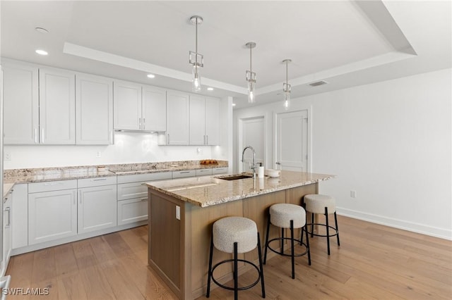 kitchen featuring a kitchen island with sink, white cabinetry, pendant lighting, and a raised ceiling