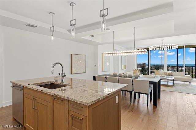 kitchen with pendant lighting, sink, a kitchen island with sink, stainless steel dishwasher, and a raised ceiling