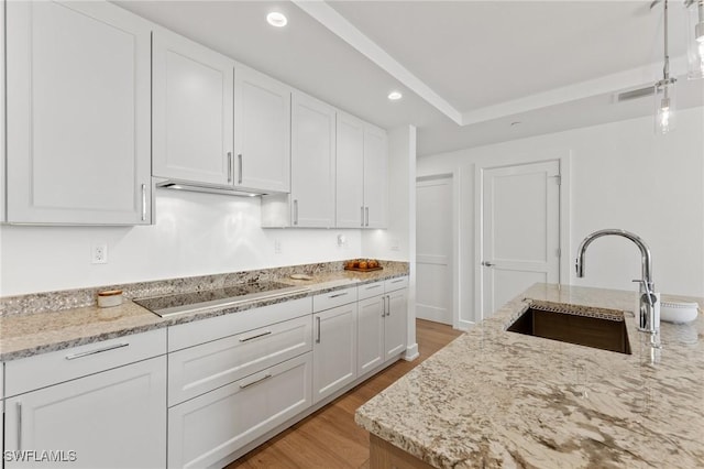 kitchen with sink, light hardwood / wood-style flooring, black electric stovetop, light stone countertops, and white cabinets