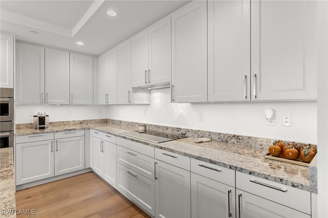 kitchen with black electric stovetop, light stone countertops, white cabinets, and light wood-type flooring