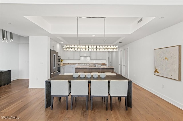 kitchen with a raised ceiling, hanging light fixtures, a center island with sink, and light hardwood / wood-style floors