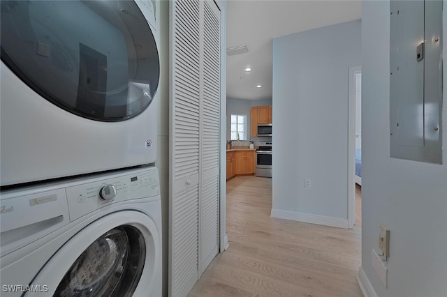 laundry room featuring light hardwood / wood-style floors, stacked washing maching and dryer, and electric panel