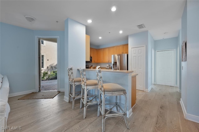 kitchen featuring stainless steel appliances, a breakfast bar area, light hardwood / wood-style flooring, and kitchen peninsula