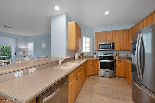 kitchen with appliances with stainless steel finishes, light wood-type flooring, kitchen peninsula, and sink