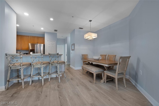 kitchen featuring hanging light fixtures, kitchen peninsula, a breakfast bar, stainless steel refrigerator with ice dispenser, and light hardwood / wood-style flooring