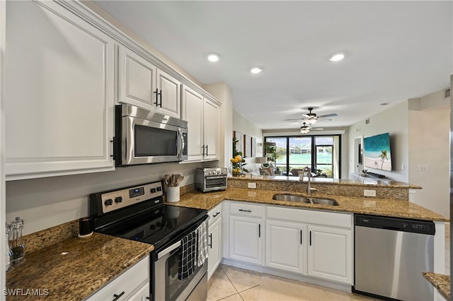 kitchen with white cabinetry, sink, stainless steel appliances, kitchen peninsula, and dark stone counters