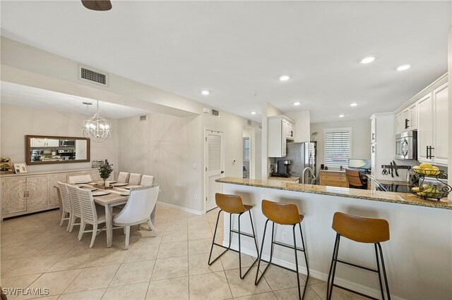 kitchen featuring kitchen peninsula, appliances with stainless steel finishes, light stone counters, white cabinetry, and a chandelier