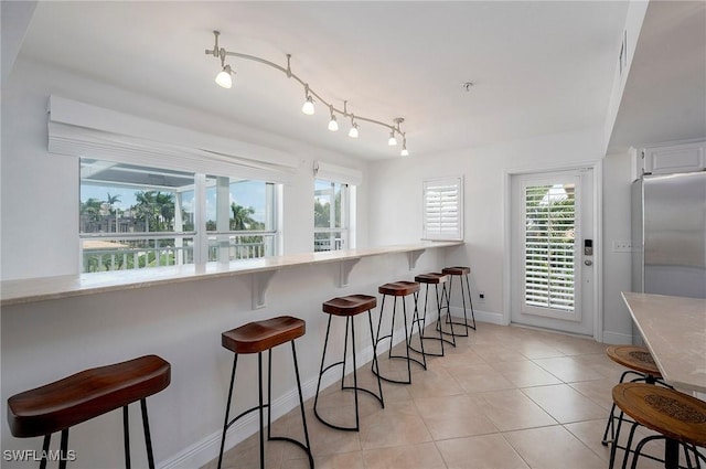 kitchen with a breakfast bar, white cabinets, light tile patterned flooring, kitchen peninsula, and stainless steel refrigerator