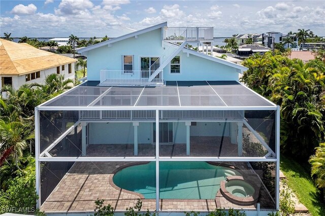 rear view of property featuring a balcony, glass enclosure, a patio area, and a pool with hot tub