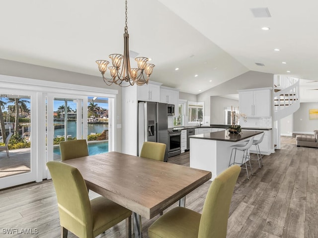 dining area with sink, a chandelier, vaulted ceiling, a water view, and light wood-type flooring