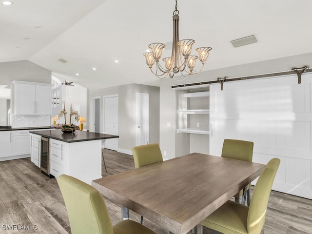 dining space featuring ceiling fan with notable chandelier, hardwood / wood-style floors, a barn door, and beverage cooler