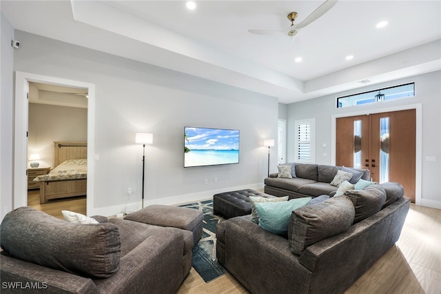 living room with ceiling fan, light hardwood / wood-style flooring, and a raised ceiling