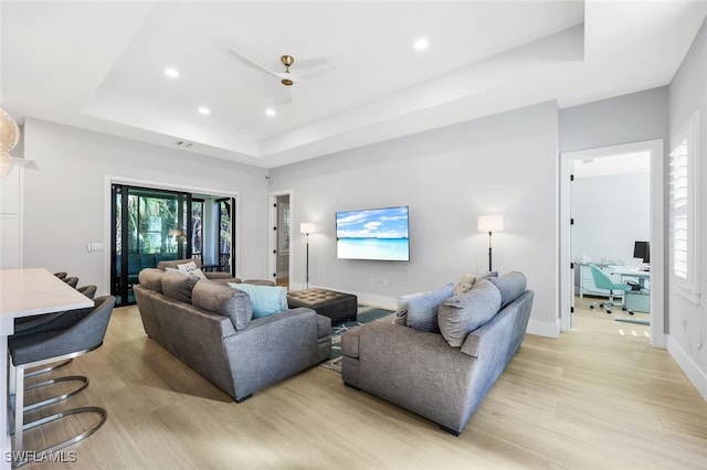 living room featuring light wood-type flooring, ceiling fan, and a tray ceiling