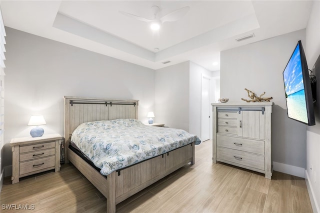 bedroom with ceiling fan, a tray ceiling, and light hardwood / wood-style flooring