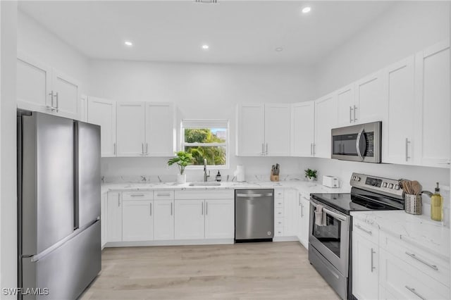 kitchen with sink, white cabinets, light hardwood / wood-style flooring, light stone countertops, and appliances with stainless steel finishes