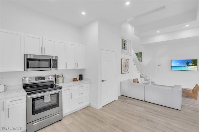 kitchen featuring white cabinetry, light stone counters, light hardwood / wood-style flooring, and appliances with stainless steel finishes