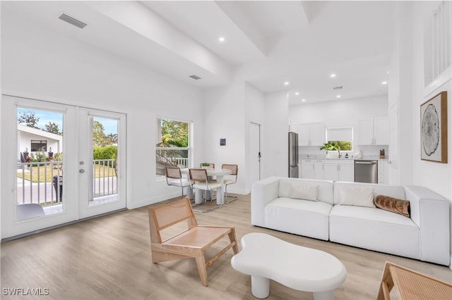 living room featuring sink, a high ceiling, french doors, and light hardwood / wood-style floors