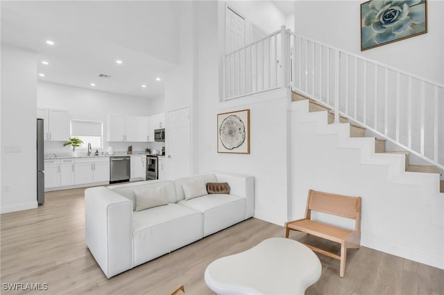 living room featuring sink, light hardwood / wood-style floors, and a high ceiling