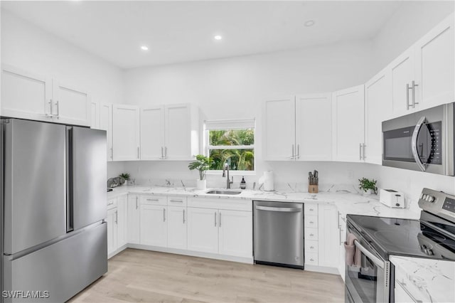 kitchen with appliances with stainless steel finishes, white cabinets, light stone counters, and sink