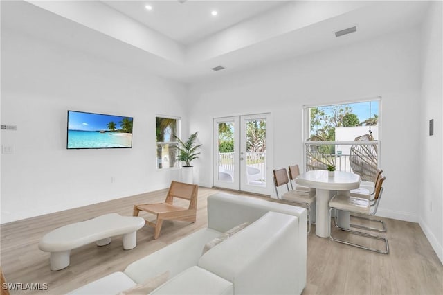 living room featuring a towering ceiling, french doors, and light hardwood / wood-style floors