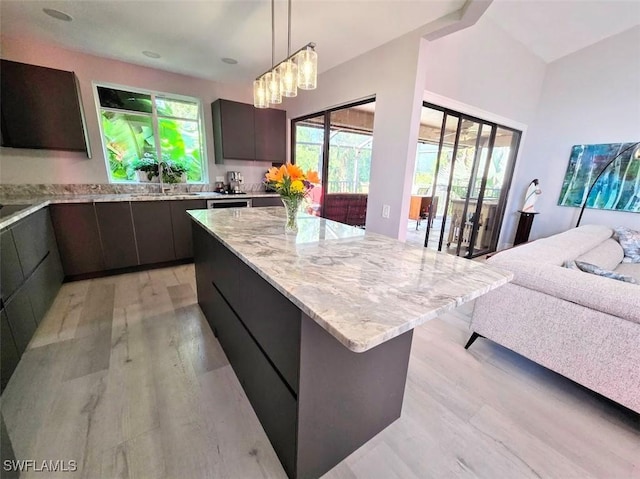 kitchen with dark brown cabinetry, decorative light fixtures, a center island, light hardwood / wood-style flooring, and light stone countertops