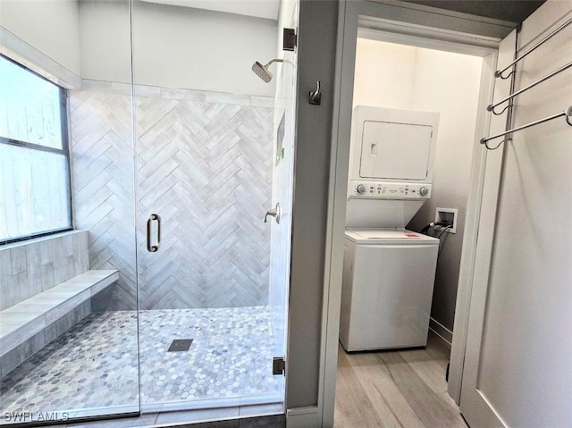 bathroom featuring an enclosed shower, stacked washer and dryer, hardwood / wood-style flooring, and a healthy amount of sunlight