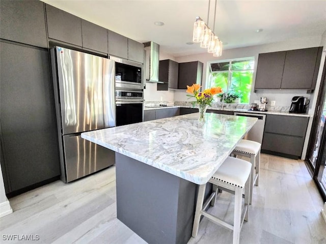 kitchen with a center island, a kitchen breakfast bar, wall chimney range hood, decorative light fixtures, and stainless steel appliances